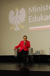 Wiceminister Edukacji Narodowej na scenie, odpowiadająca przez mikrofon na pytania uczestników spotkania. W tle na ekranie wyświetlone logo Ministerstwa Edukacji Narodowej.