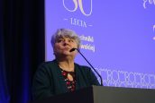 Małopolska Kurator Oświaty dr Gabriela Olszowska stoi na scenie i przemawia do zgromadzonych do mikrofonu, podczas Święta Politechniki. Za nią wyświetlana prezentacja.