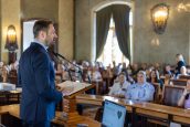 Prezydent Krakowa Aleksander Miszalski stoi na scenie w trakcie swojego przemówienia. Przed nim wsłuchana publiczność, trzyma w rękach list.