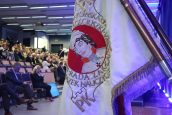 Sztandar Politechniki Krakowskiej, przedstawiający jej patrona - Tadeusza Kościuszko, na dalszym planie zgromadzone osoby na uroczystości, które siedzą na swoich miejscach.