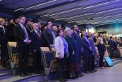 Zaproszeni goście na wydarzenie, w tym Małopolska Kurator Oświaty, stoją na baczność i śpiewają hymn, przed oficjalnym rozpoczęciem uroczystości.