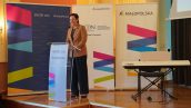 II Małopolska Wicekurator Oświaty Katarzyna Mitka stoi na scenie i przemawia do publiczności, za nią kilka rollupów oraz po prawej stronie sprzęt muzyczny przygotowany do występu artystycznego.