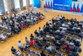 Zdjęcie przedstawiające sale, gdzie odbywała się konferencja, zaproszeni goście siedzą na krzesłach po lewej i prawej stronie, na dalszym planie prelegent mówiący do publiczności ze sceny.