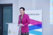 II Małopolska Wicekurator Oświaty Katarzyna Mitka stoi na scenie i przemawia do publiczności, w tle baner reklamowy Małopolski.