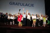 Jedna ze szkół biorąca udział w konkursie. Jedna z osób trzyma w ręku puchar za zdobycie pierwszego miejsca, za nimi wyświetlony napis gratulacyjny.