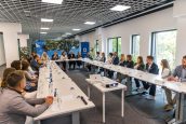 Zdjęcie przedstawiające wszystkich uczestników wydarzenia, którzy siedzą przy stole i debatują o temacie spotkania.