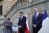 Konsul Francji w trakcie swojego wystąpienia, stoi przed mikrofonem. Za nim flagi Polski oraz Francji.