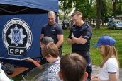 Policjanci stoją obok dzieci, które pojawiły się na pikniku i prezentują im m.in broń, którą się posługują w trakcie pracy.
