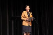 II Małopolska Wicekurator Oświaty Katarzyna Mitka w trakcie czytania okolicznościowego listu od Małopolskiej Kurator Oświaty, stojąc na scenie przed mikrofonem.