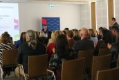 Na bliższym planie zgromadzona publiczność w trakcie spotkania, na scenie szef Małopolskiego Centrum Doskonalenia Nauczycieli ze swoim wystąpieniem.