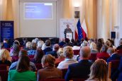 Wiceministra Katarzyna Lubnauer stoi na scenie przed mikrofonem w trakcie swojego wystąpienia, na bliższym planie siedzą zaproszeni goście, w tym kuratorzy oświaty. Za Lubnauer m.in prezentacja i baner reklamowy.
