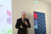 I Małopolski Wicekurator Oświaty Artur Pasek stoi na scenie i przemawia do mikrofonu. Za nim baner reklamowy.