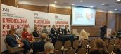 Panel dyskusyjny w trakcie konferencji o Kardiologii Prewencyjnej. Prelegenci siedzą na krzesłach i są zwróceni ku prowadzącemu, który stoi i trzyma mikrofon.