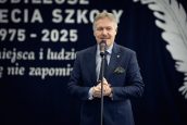 Małopolski Wicekurator Oświaty Artur Pasek stoi na scenie przed mikrofonem z założonymi dłońmi i przemawia do zgromadzonych gości w trakcie części oficjalnej wydarzenia.