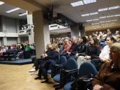 Widok licznie zgromadzonej publiczności, która siedzi w fotelach i słucha jednego z wykładów. Niektórzy notują, inni trzymają także kubki.