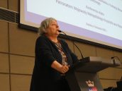 Małopolska Kurator Oświaty dr Gabriela Olszowska stoi na scenie, trzymając się pulpitu. Przed nią ustawiony mikrofon, do którego mówi. Za nią wyświetlona prezentacja z nazwą konferencji.