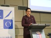 II Małopolska Wicekurator Oświaty Katarzyna Mitka w trakcie rozpoczęcie wydarzenia, stoi na scenie i przemawia do mikrofonu, witając gości. Za nią ustawiony rollup Kuratorium Oświaty.