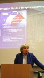 Małopolska Kurator Oświaty dr Gabriela Olszowska w trakcie wystąpienia. Z tyłu wyświetlany plakat z programem konferencji.