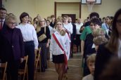Młodzież szkolna ubrana w odświętne stroje idzie przez salę gimnastyczną, wprowadzając Sztandar Szkoły.