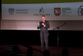 I Małopolski Wicekurator Oświaty Artur Pasek przemawia do mikrofonu na scenie, za nim wyświetlona prezentacja.
