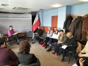 Wicekurator Katarzyna Mitka siedzi przy biurku. Wokół siedzą pozostali uczestnicy spotkania. W tle widoczna flaga Polski oraz ścianka z napisem Kuratorium Oświaty w Krakowie.