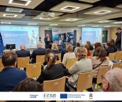 Widok ogólny sali, w której odbyło się wydarzenie. Na scenie jeden z prelegentów trzymający mikrofon.