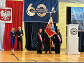 Na zdjęciu widoczny Sztandar Szkoły i oraz trójkę uczniów. Po lewej stronie prowadzący wydarzenie stoją obok siebie