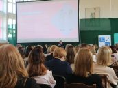 Widok zgromadzonej publiczności w trakcie wydarzenia, która siedzi na krzesłach. Na dalszym planie jedno z wystąpień.