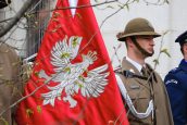 Zdjęcie przedstawiające żołnierzy, stojących w trakcie uroczystości. Jeden z nich trzyma sztandar, na którym widnieje orzeł.