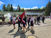 Przemarsz z kościoła do sali. Na bliższym planie odświętnie ubrani uczniowie trzymający Sztandar a za nimi pozostali uczestnicy wydarzenia.