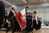 Biało-czerwony Sztandar Uczelni wnoszony przez studentów w trakcie uroczystości. Studenci idą w stronę sceny.