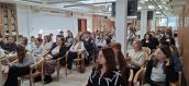 Uczestnicy spotkania siedzący na krzesłach w sali z kolumnami.