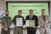 Wicekurator Artur Pasek oraz przedstawiciele ZHP z osobą wyróżnioną. W tle slajd z napisem Szkoła Przyjazna Harcerstwu.