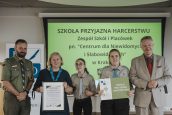 Wicekurator Artur Pasek oraz przedstawiciele ZHP z osobą wyróżnioną. W tle slajd z napisem Szkoła Przyjazna Harcerstwu.