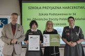 Wicekurator Artur Pasek oraz przedstawiciele ZHP z osobą wyróżnioną. W tle slajd z napisem Szkoła Przyjazna Harcerstwu.